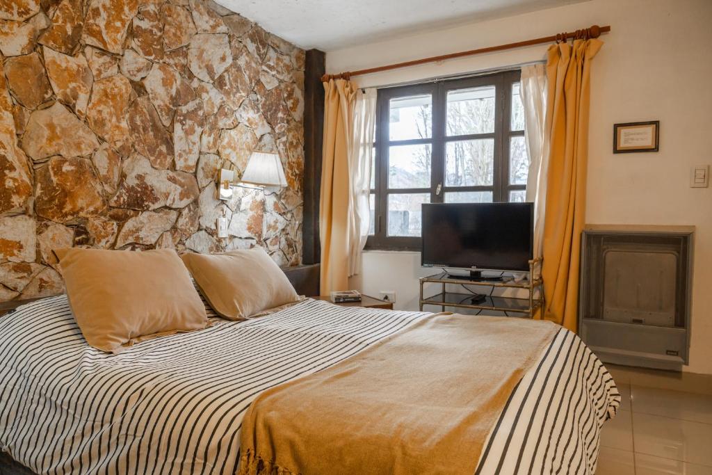 quarto da Posada Del Fin Del Mundo com uma parede de pedra, uma cama de casal e uma janela quadriculada