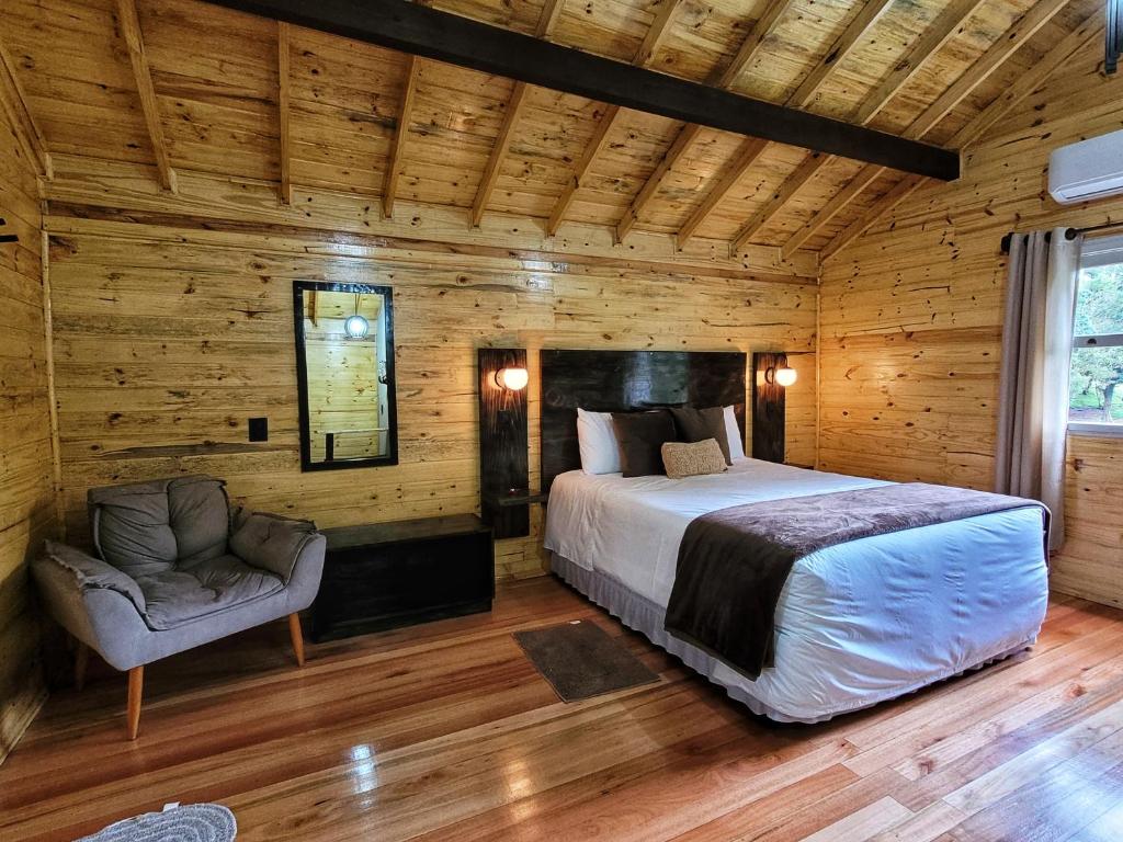 vista interna do chalé Pousada Cardoso com madeira exposta, cama de casal à direta, uma poltrona cinza à esquerda e um pequeno espelho preso à parede entre os dois