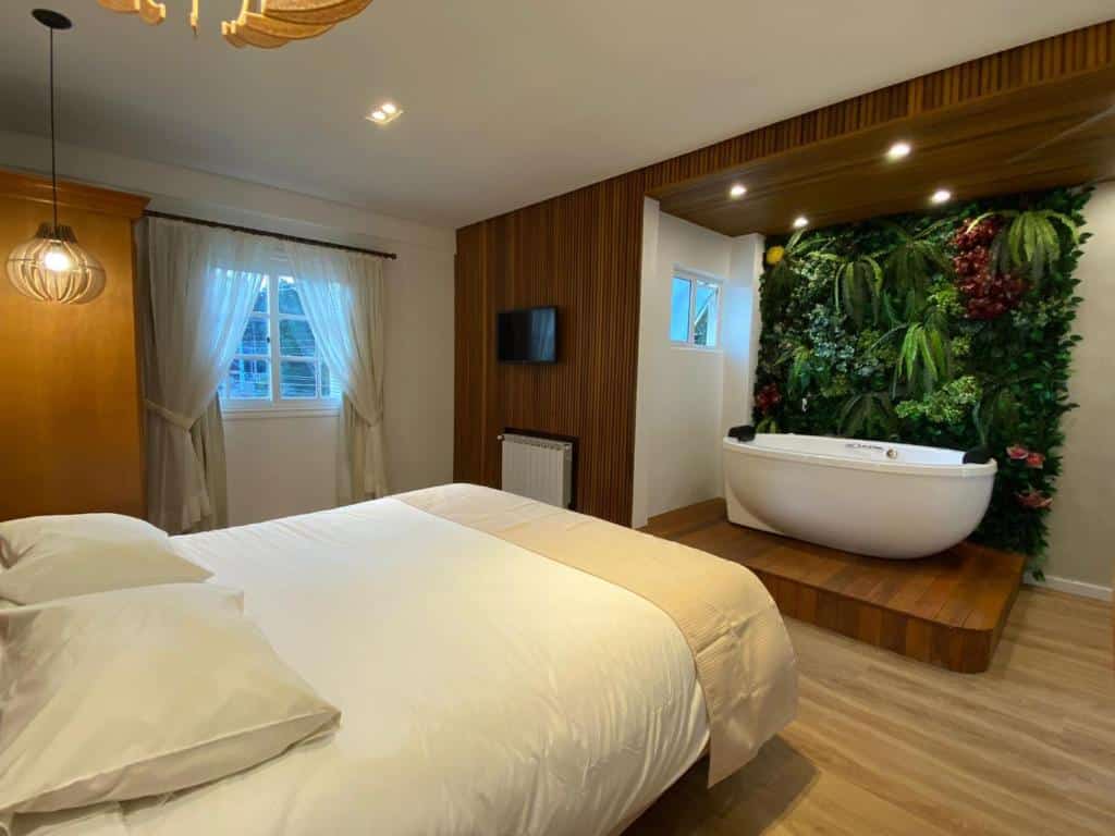 Quarto da Pousada Dom Alfredo José com uma banheira, uma cama de casal, uma janela com cortinas e um chão de madeira, para representar pousadas baratas em Campos do Jordão