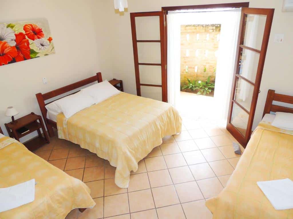 Quarto na Pousada Mosaico Brasil - Maresias com uma cama de casal e duas de solteiro, além de uma varanda térrea e duas mesinhas de cabeceira