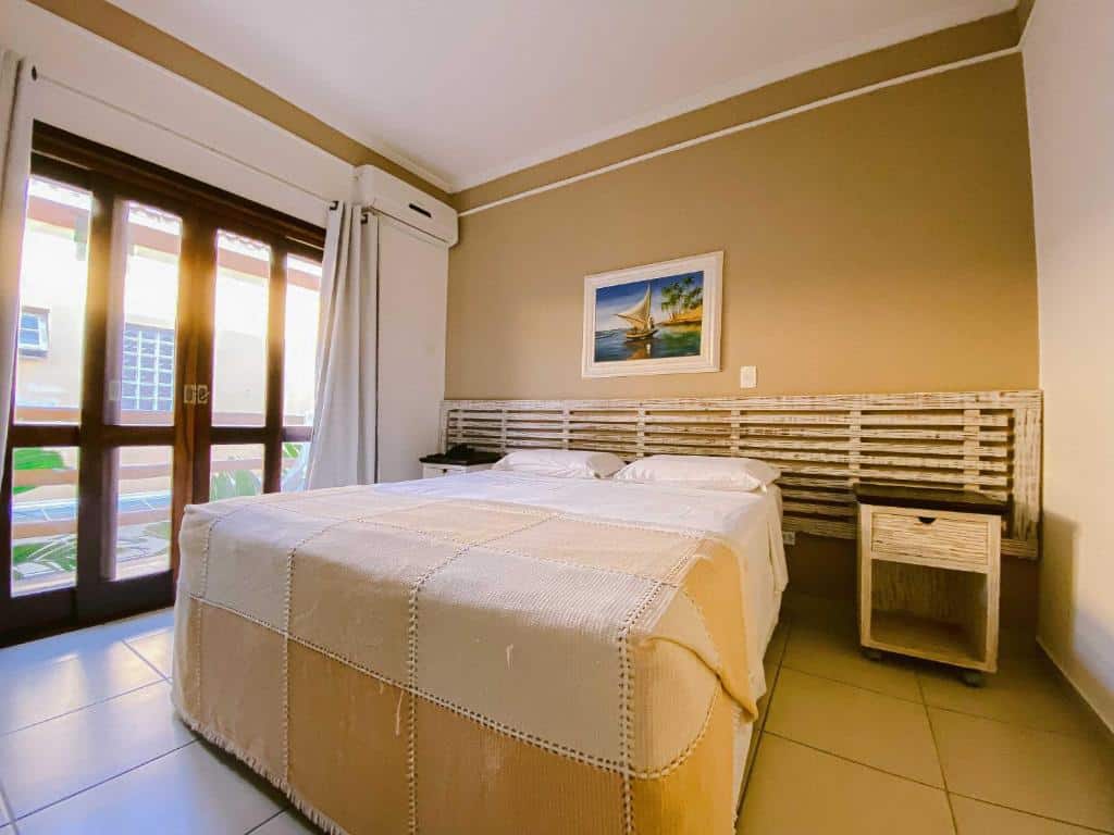 Quarto da Pousada Porto Mare com cama de casal, uma varanda térrea com cortinas, duas mesinhas de cabeceira e um ar-condicionado de teto, para representar pousadas pé na areia em Maresias