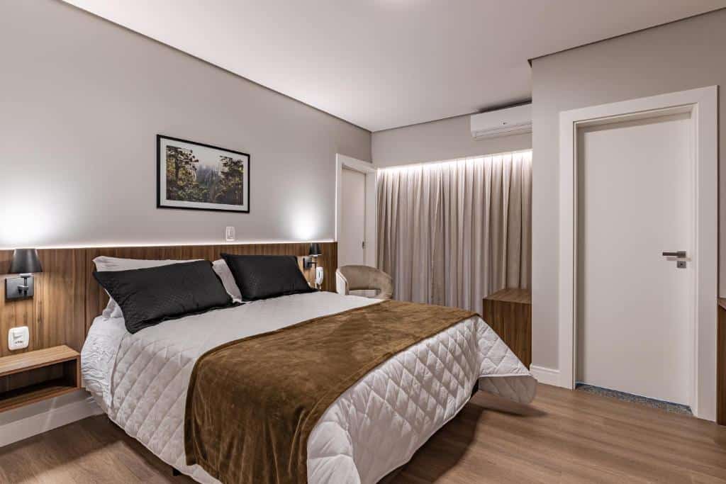 quarto da Pousada Serra Verde com uma cama de casal à esquerda, um quadro de natureza sobre a cabeceira, paredes pintadas em cinza e uma porta branca à direita
