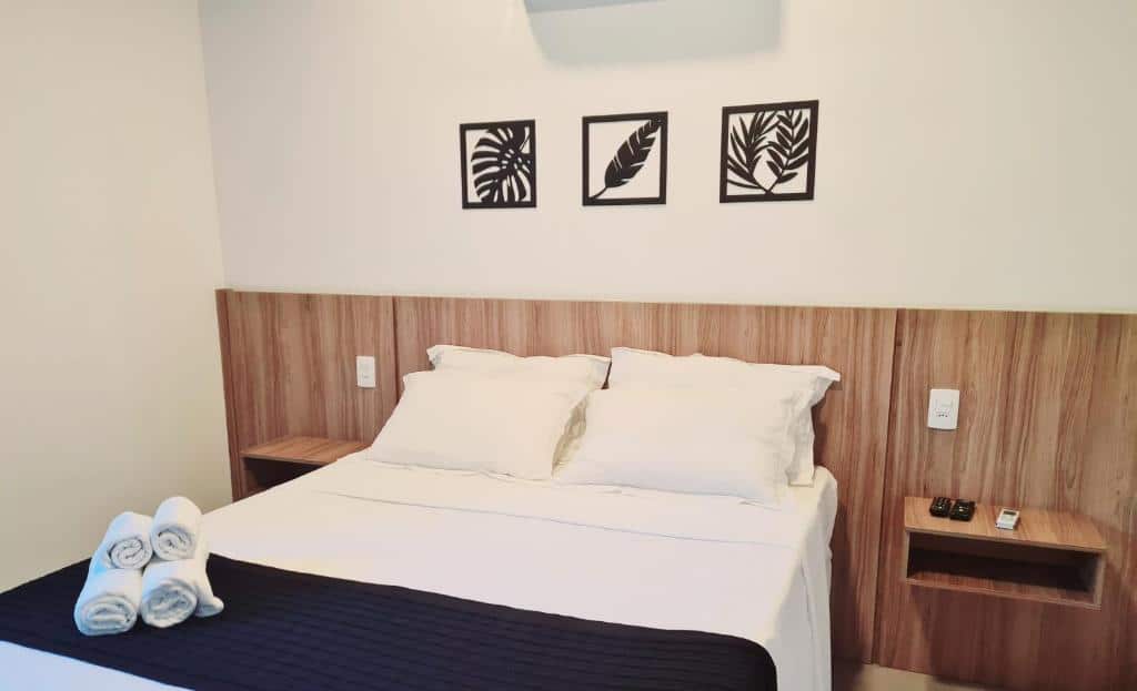 Quarto da Pousada Vila Ipuan com cama de casal ao centro, duas cômodas ao lado cama e quatro toalhas em cima da cama.