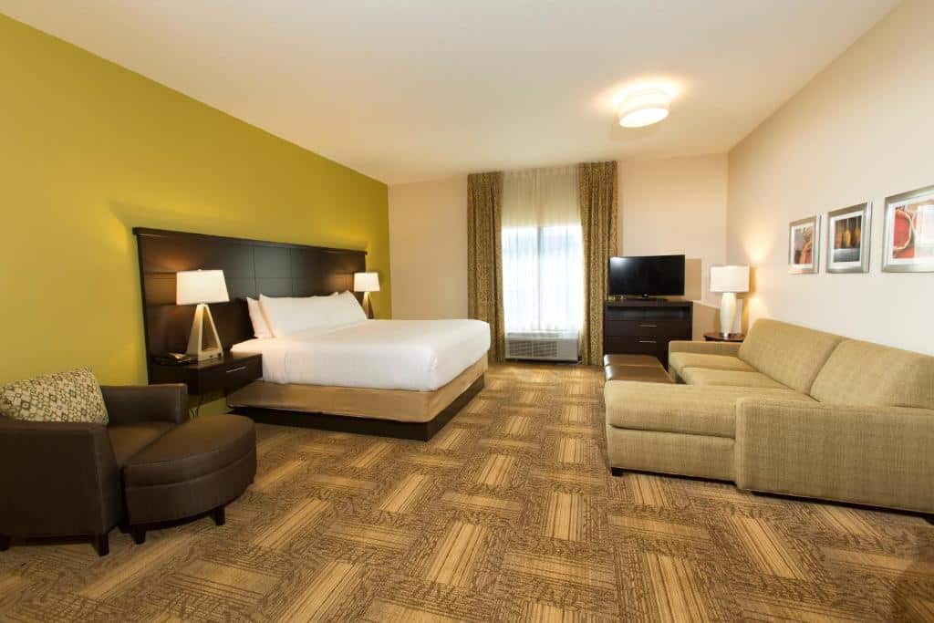 Quarto amplo do Staybridge Suites Orlando at SeaWorld, an IHG Hotel com uma cama de casal, uma janela com cortinas, um móvel com uma televisão, um sofá que abre, e uma poltrona marrom de couro