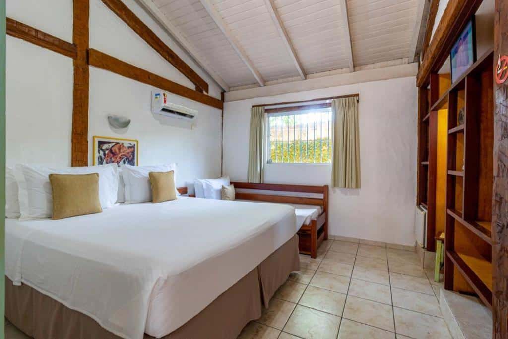 Quarto da Pousada Tambayba com cama de casal no centro do quarto, do lado esquerdo sofá cama e janela com cortinas bege.