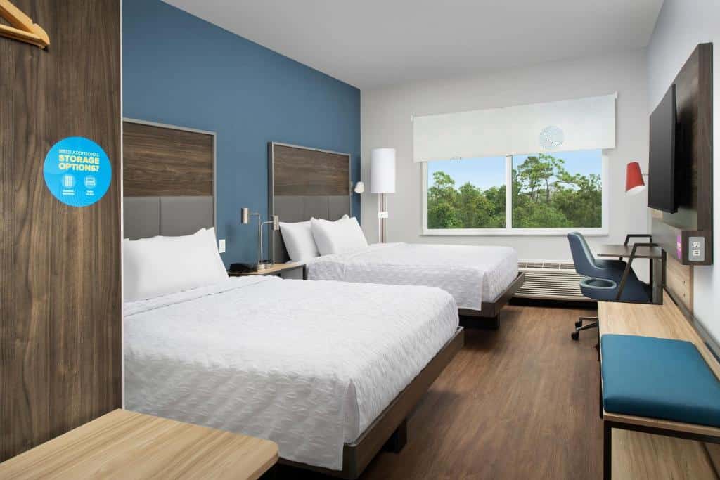Quarto do Tru By Hilton Orlando Convention Center com uma cama de casal e uma de solteiro, há um ampla janela com persiana, uma pequena mesa de escritório, uma televisão e o chão é de madeira