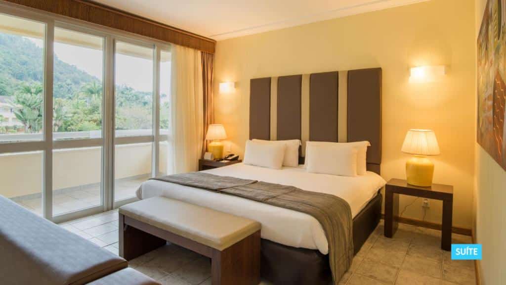 Quarto do Vila Galé Eco Resort Angra - All Inclusive com cama de casal, varanda ampla, duas mesinhas com abajures nas laterais da cama, para representar resorts em Angra dos Reis