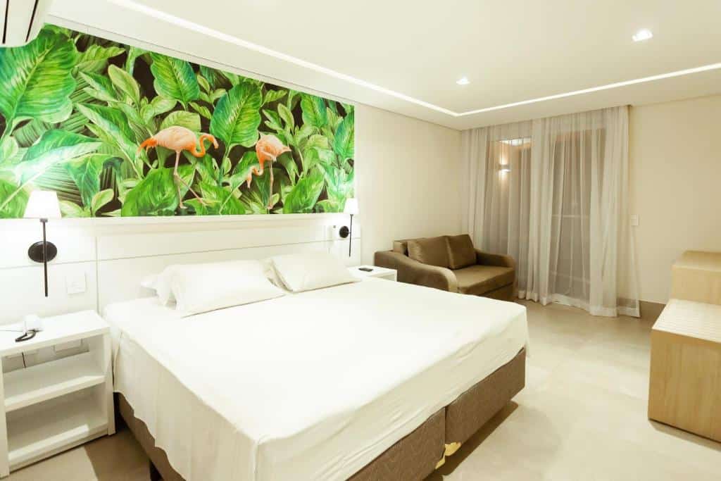 Quarto da Vistabela Resort & Spa com cama de casal, duas comodas de madeiras branca, sofá de dois lugares do lado esquerdo e portas com cortinas brancas.