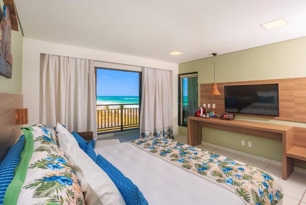 Quarto do Vivá Porto de Galinhas Resort com uma sacada com vista para a praia, uma cama de casal e um móvel de madeira com uma televisão