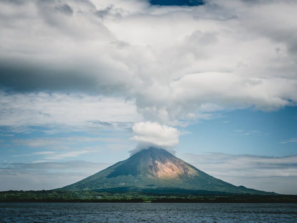 Vista de um vulcão em Nicarágua saindo fumaça em seu topo, com natureza em volta e mar à frente. Imagem para ilustrar o post de chip de celular Nicarágua