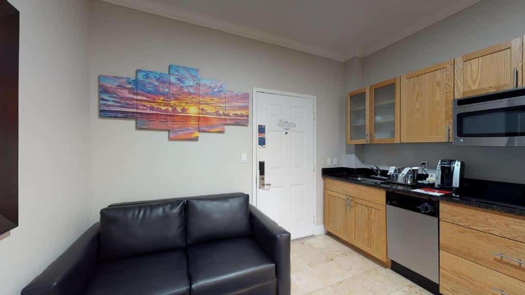Sala de estar do Nuvo Suites Hotel – Miami / Doral com cozinha. Sofá de couro do lado esquerdo e do lado direito armário de madeira com pia, fogão. Representa hotéis com cozinha em Miami.