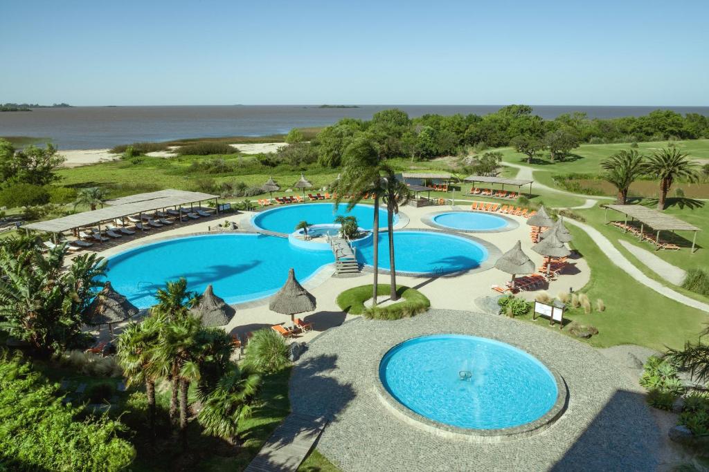 Diversas piscinas em formato arredondado do Sheraton Colonia Golf & Spa Resort, cercado por amplos jardins que se estendem até a margem de um rio, para representar hotéis em Colonia del Sacramento