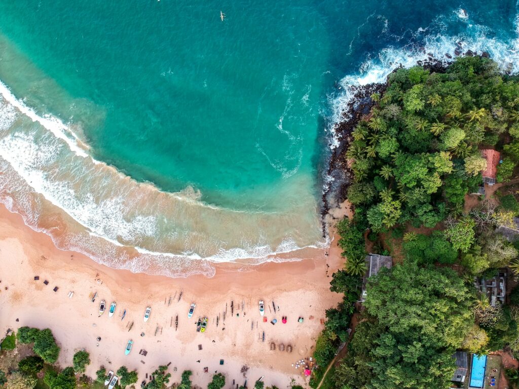 Vista aérea de uma pequena praia no Sri Lanka com muitas árvores por perto, mar verde claro e areia em tom de bege