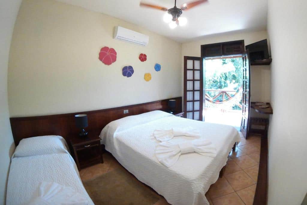 Quarto do chalé standard do Vale do Sonho Hotel, de 40 m², com uma cama de solteiro, uma de casal, ar-condicionado, ventilador de teto e varanda com rede