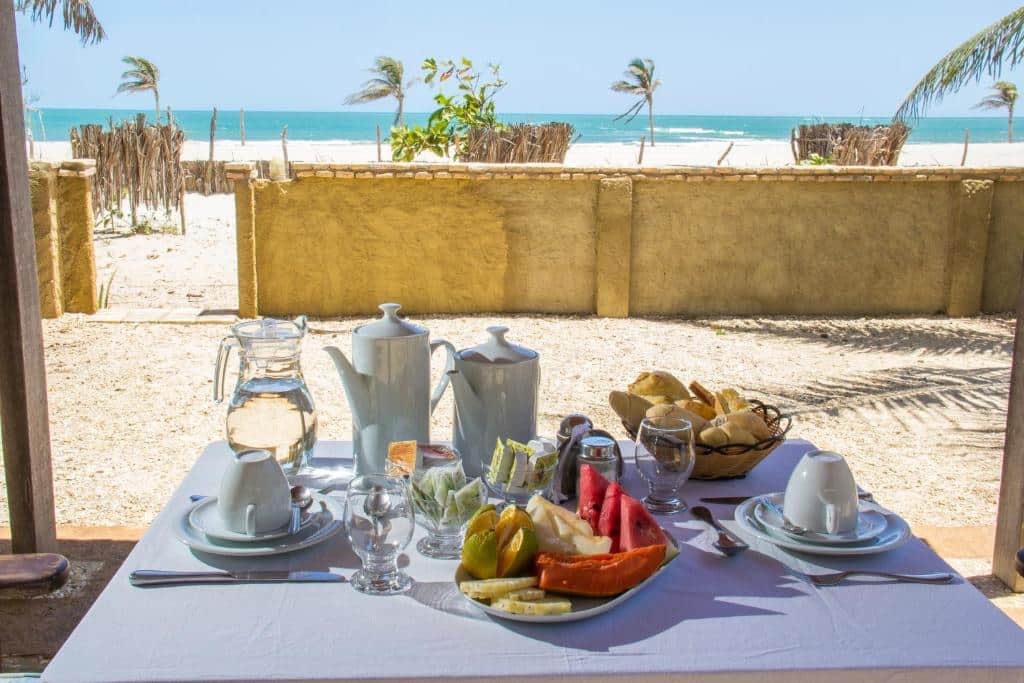 Mesa com café da manhã à beira-mar do Villa del Mar Praia Hotel. Há um muro reservando a área do hotel e a praia tem águas cristalinas e areia branca