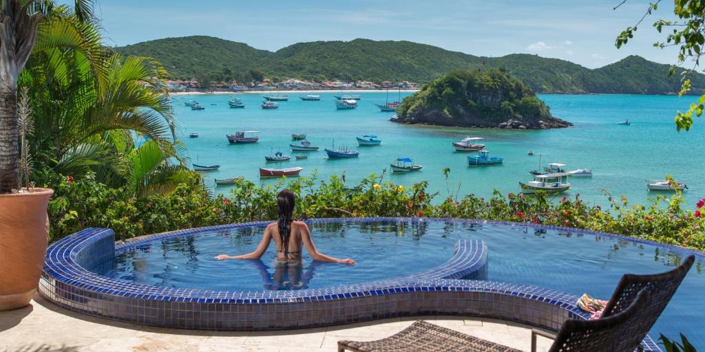 Uma piscina pequena com borda infinita da Vila D’Este Handmade Hospitality Hotel com vista direta para o mar com muitos barcos e as montanhas ao fundo