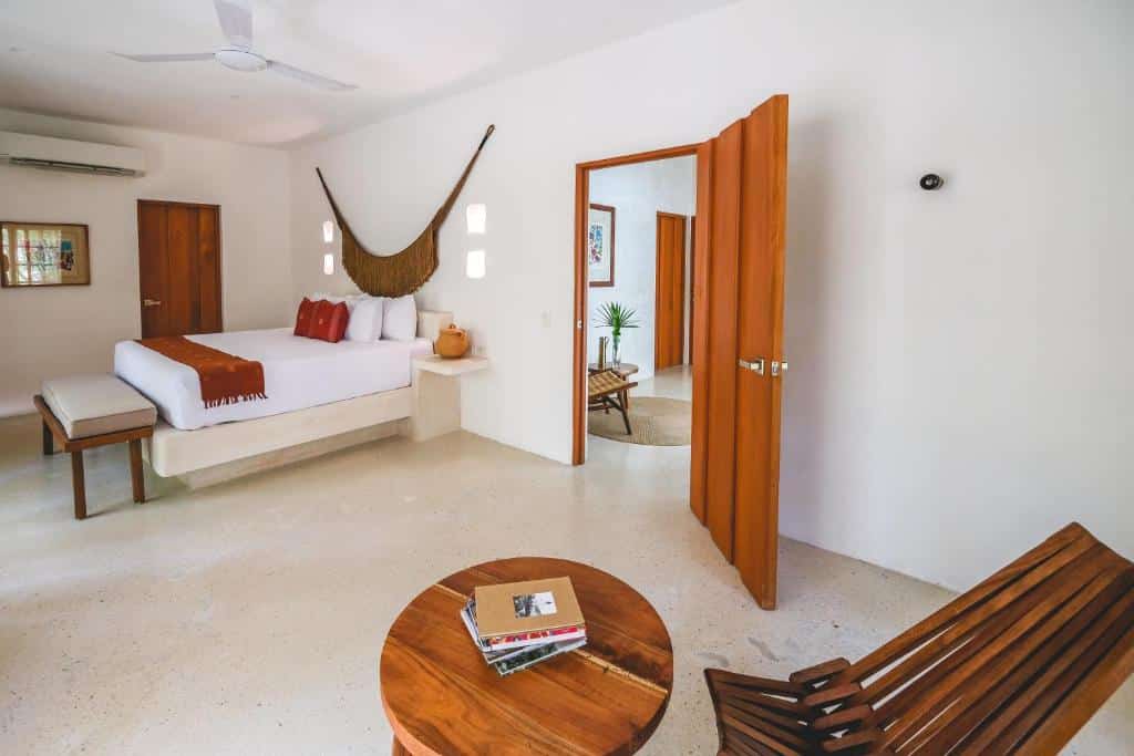 Quarto de Wakax Hacienda, de 94 m²,  com cama de casal, mesa redonda com uma cadeira de madeira e porta dando acesso a outro cômodo do local