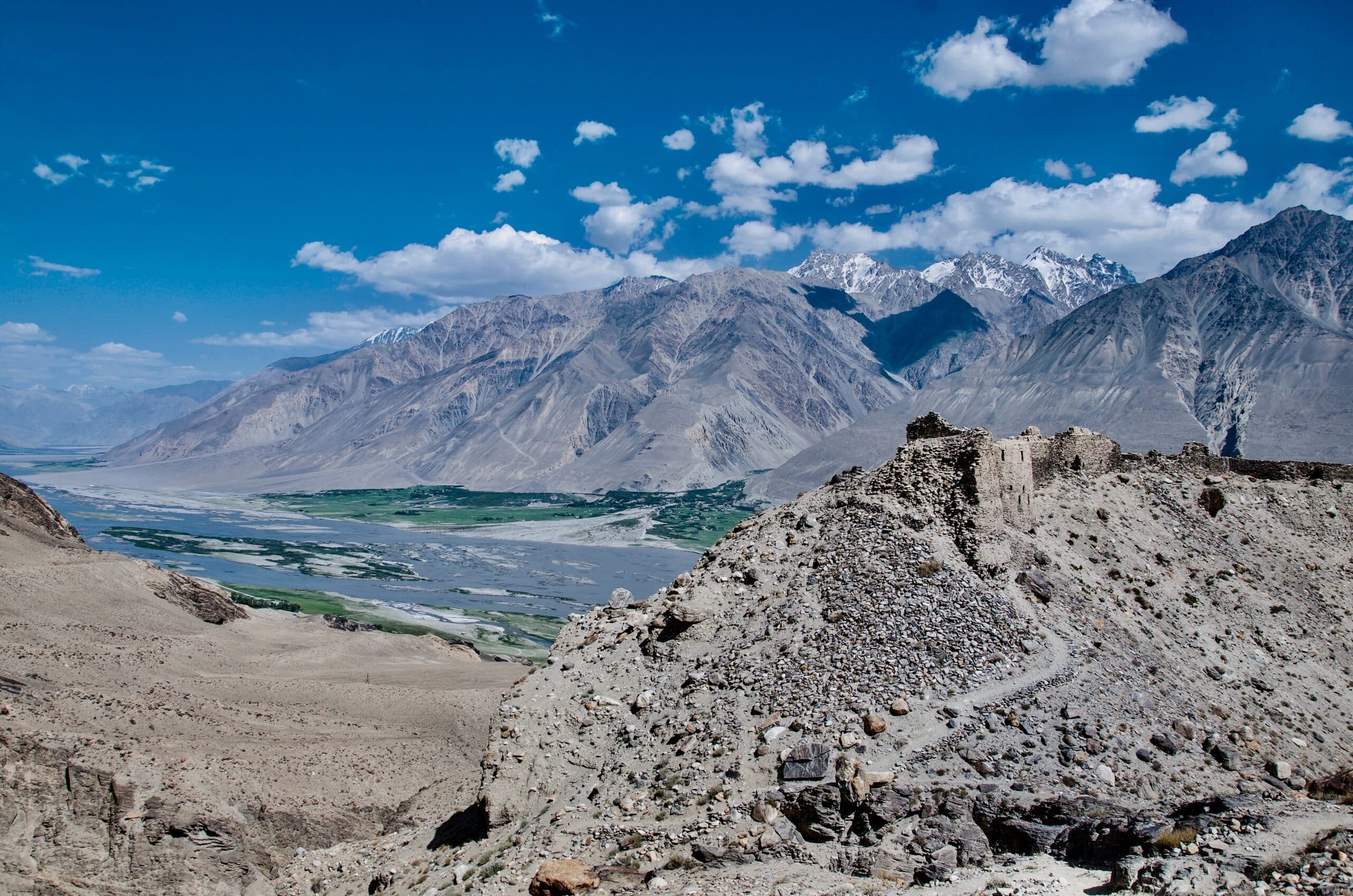 Vista de Yamchun Fort, Tajiquistão, durante o dia, que possui montanhas rochosas e um pequeno lago na área central.