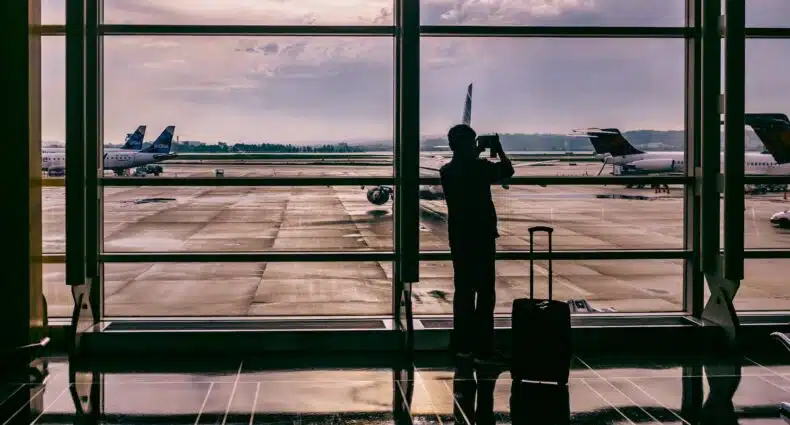 vista do Ronald Reagan Washington National Airport, Arlington ao entardecer com uma pessoa e uma mala segurando um celular em que tira fotos através do vidro de aviões em um espaço aberto
