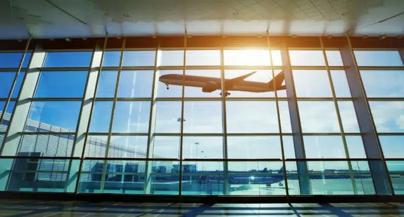 foto do Aeroporto Afonso Pena, de Curitiba, em que é possível ver um avião passando por uma janela de vidro enorme