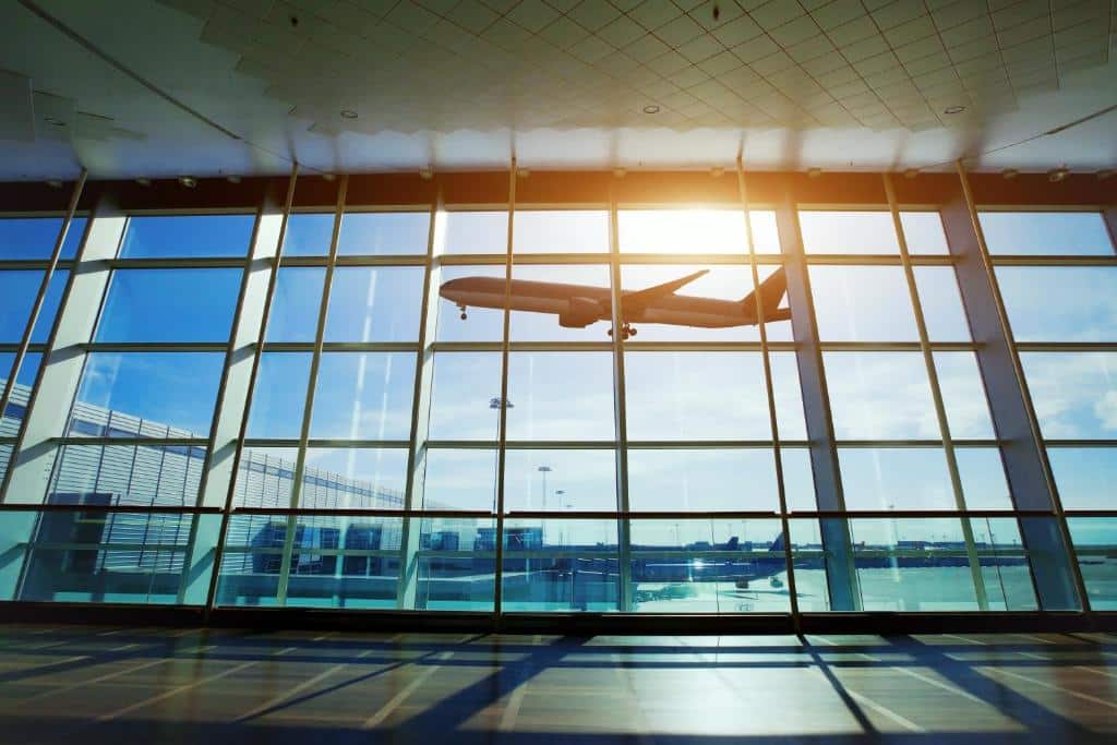 foto do Aeroporto Afonso Pena, de Curitiba, em que é possível ver um avião passando por uma janela de vidro enorme