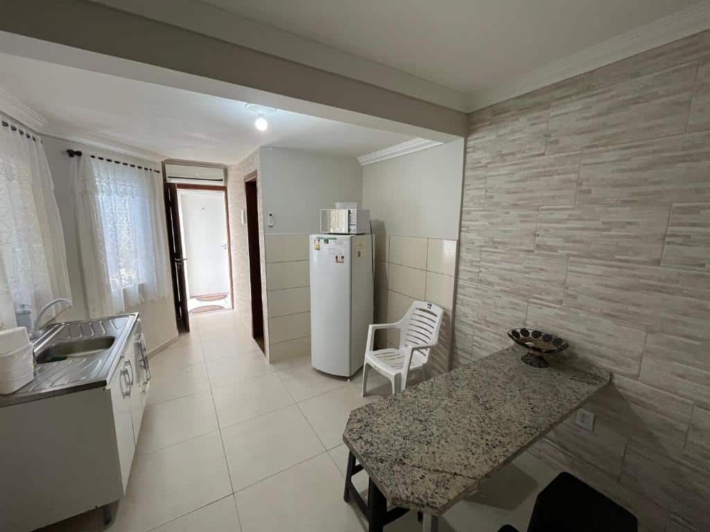 apartamento da Pousada Marques Floripa, um dos hotéis perto do Aeroporto de Florianópolis, com cozinha e sala conjugadas, com pia, geladeira e mesa de mármore com cadeiras