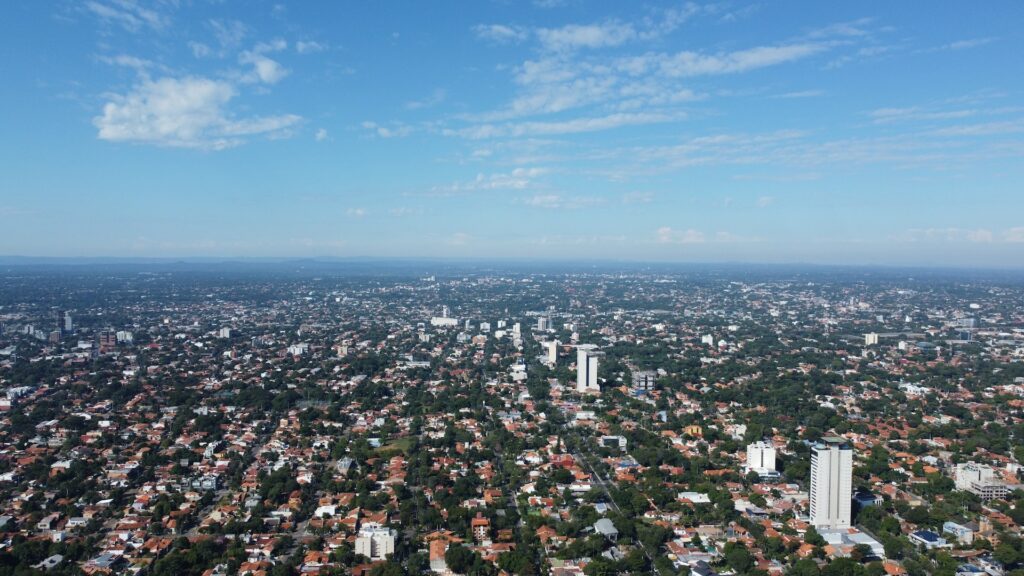 Vista aérea da cidade de Assunção no Paraguai. Várias construções, como casas e prédios, cercados por vegetação em um dia de céu azul.