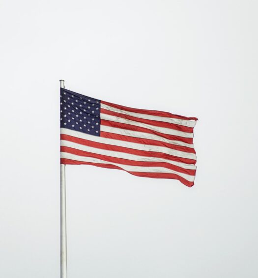 Bandeira dos EUA na Embaixada do país norte-americano na Alemanha, totalmente estendida devido ao vento em um dia nublado, para ilustrar a capa do post sobre entrevista do visto americano