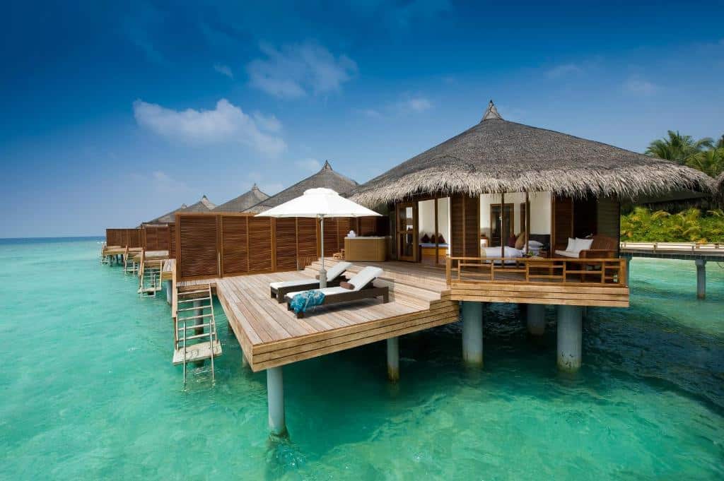 bangalô do Kuramathi Maldives, acima da água de águas cristalinas com espreguiçadeiras e quarto