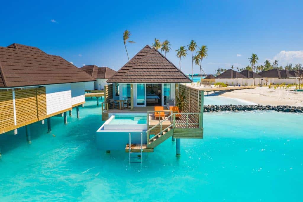 bangalô acima do mar de águas cristalinas no Sun Siyam Olhuveli, um dos resorts nas Maldivas, com uma escadinha que liga a praia ao quarto, com hidro e cadeiras nas varandas