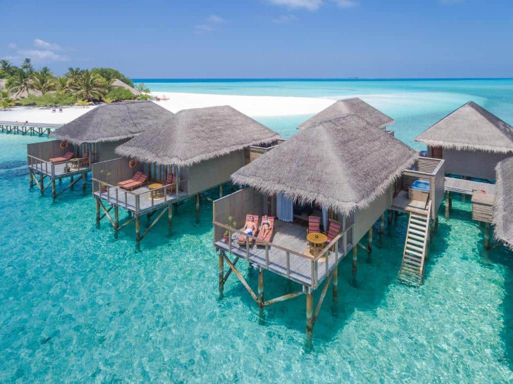 vista de bangalôs iguais acima da água verde cristalina no Meeru Island Resort & Spa, um dos resorts nas Maldivas com espreguiçadeiras e escada que desce direto para a praia