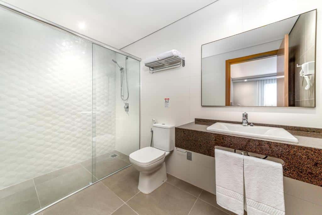 banheiro no Intercity Portofino Florianópolis, um dos hotéis perto do Aeroporto de Florianópolis, com ambientes amplos, pia mais baixa , vaso mais alto e box aberto