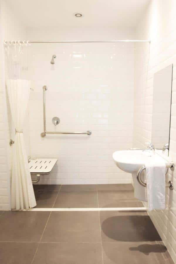 Foto de banheiro adaptado no B&B Hotels de São José dos Campos, com pia e espelho rebaixados, barras de apoio, e assento no chuveiro