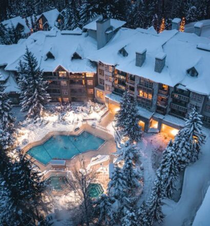 Vista aérea do Blackcomb Springs Suites by CLIQUE com uma construção coberta por neve, muitos pinheiros cobertos de neve ao redor de uma piscina aquecida ao ar livre, para representar hotéis em Whistler