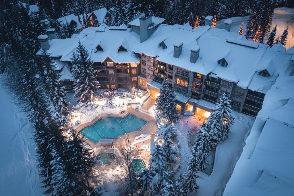 Vista aérea do Blackcomb Springs Suites by CLIQUE com uma construção coberta por neve, muitos pinheiros cobertos de neve ao redor de uma piscina aquecida ao ar livre, para representar hotéis em Whistler
