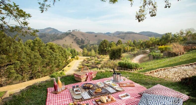 Espaço verde entre montanhas e com muitas árvores no Botanique Hotel & Spa com uma toalha estendida no gramado com um piquenique e duas almofadas