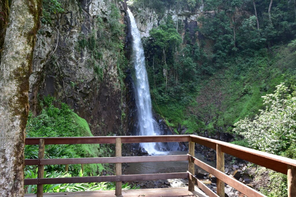 Vista da Cachoeiras Três Quedas, Brotas durante o dia com queda água no meio de rochas e área verde.