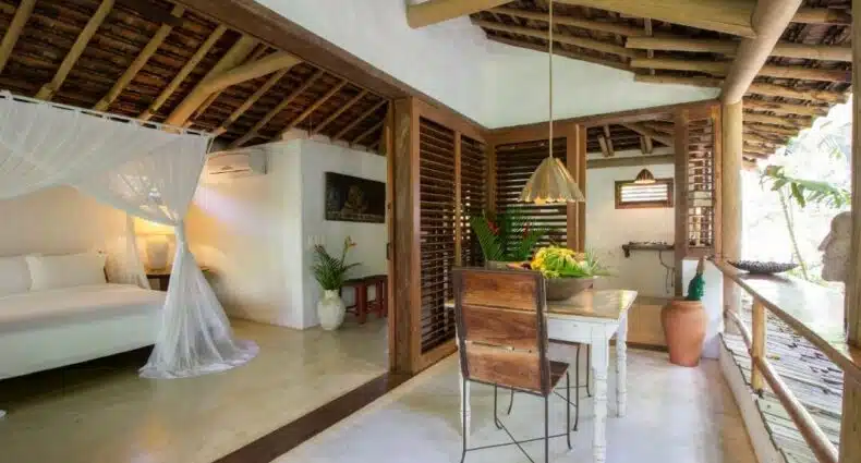 Quarto do Uxua Casa Hotel & Spa, com cama do lado esquerdo e mesa de madeira com duas cadeiras do lado direito. Representa resorts em Trancoso.