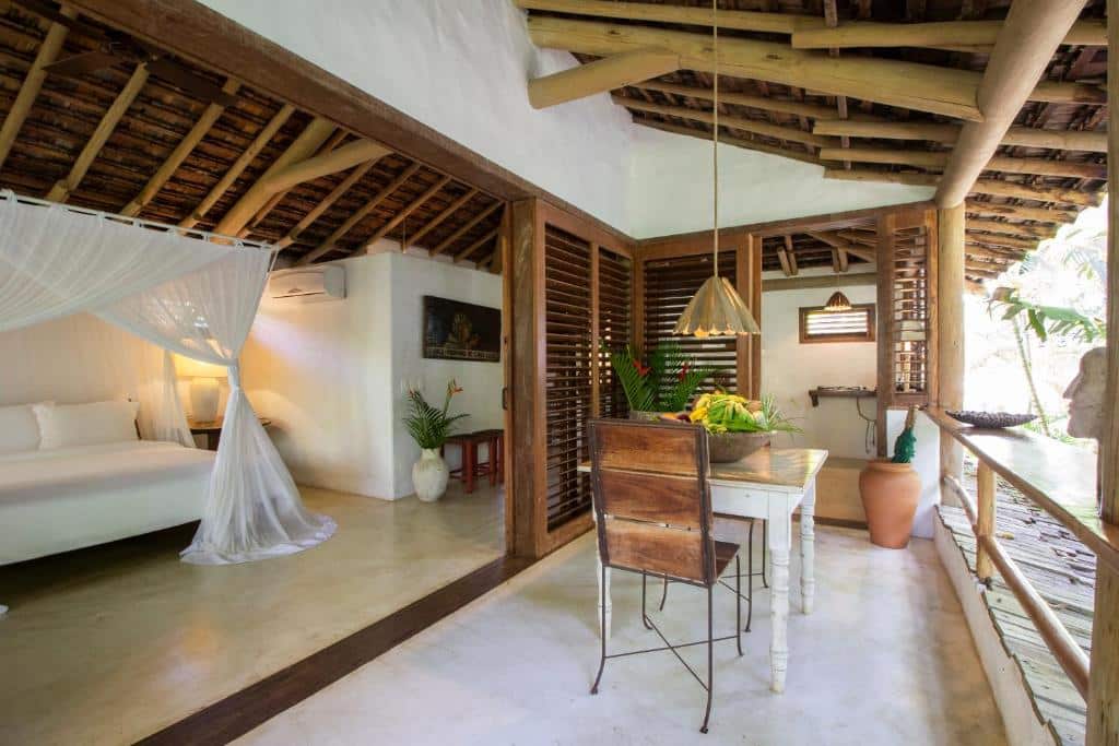 Quarto do Uxua Casa Hotel & Spa, com cama do lado esquerdo e mesa de madeira com duas cadeiras do lado direito. Representa resorts em Trancoso.