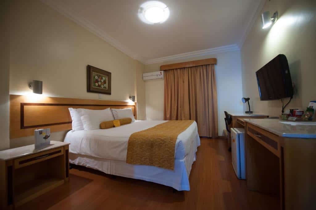 Quarto do hotel Carlton Plaza São José dos Campos, com cama de casal, cortina blecaute, ar-condicionado, TV, frigobar e mesinha de trabalho