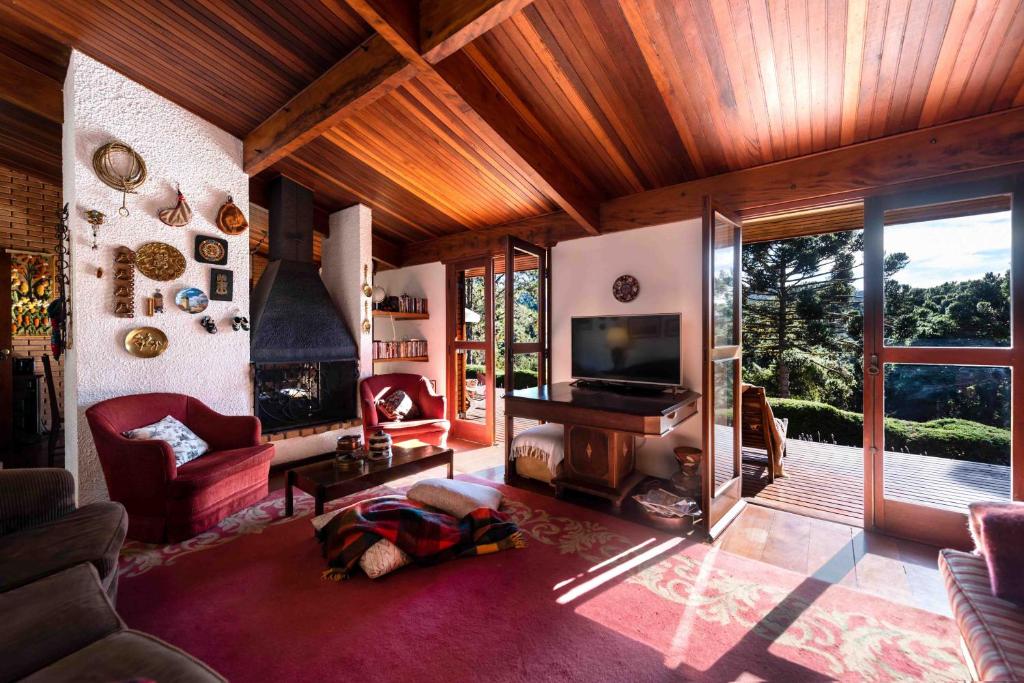 Uma sala de estar ampla na Casa Xamego Alto Padrão com pôr do sol espetacular com uma lareira, televisão, tapete vermelho, um sofá e há duas portas de vidro que levam para uma varanda aberta com vista para as montanhas