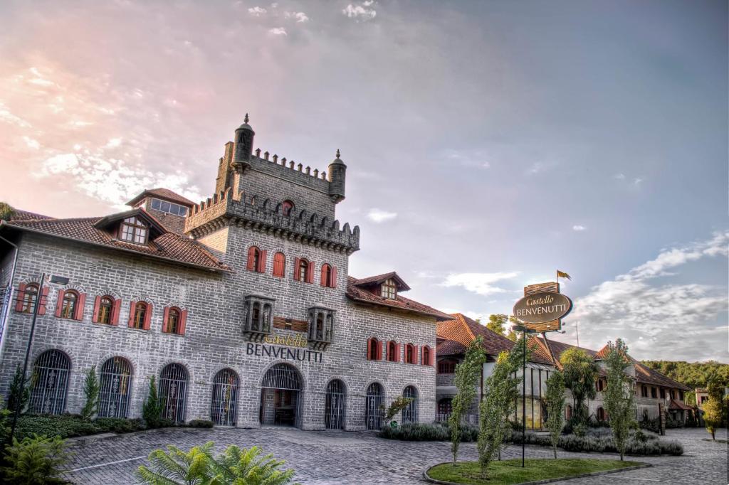 Propriedade da  Pousada Castello Benvenutti construída como um castelo medieval, em tijolos cinzas, com duas pequenas torres, janelas vermelhas e um pequeno gramado na frente, localizado em Bento Gonçalves