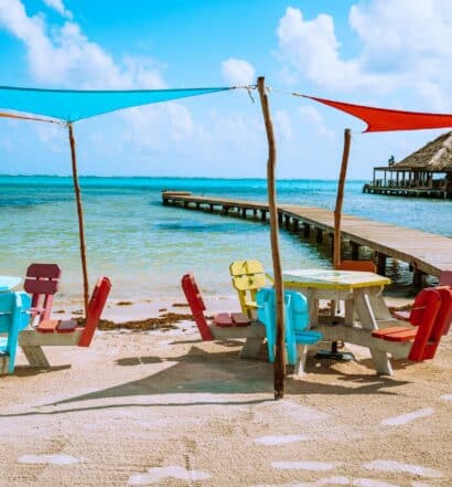 Cadeiras e mesas coloridas na faixa de areia em frente ao mar de água azul, ao lado um deck dentro da água durante o dia, ilustrando post chip celular Belize.