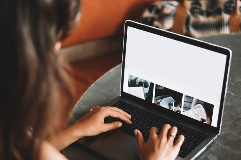 Mulher usando notebook com as duas mãos sobre o teclado dele, digitando, enquanto olha uma página da web, para ilustrar o post sobre como tirar passaporte, mais especificamente online