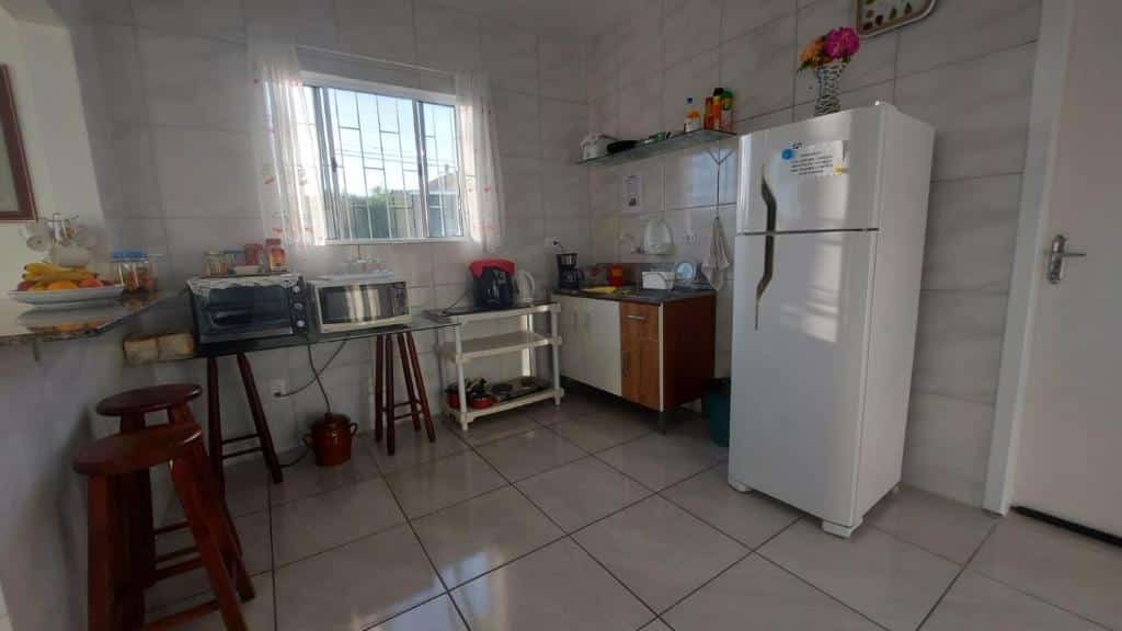 cozinha da Pousada Decarli Executiva perto do Aeroporto de Florianópolis, com geladeira, forninho, pia, e móveis de madeira e janela de vidro