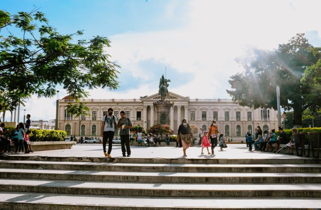 Palácio Nacional de El Salvador atrás com escadaria a frente com algumas pessoas.
