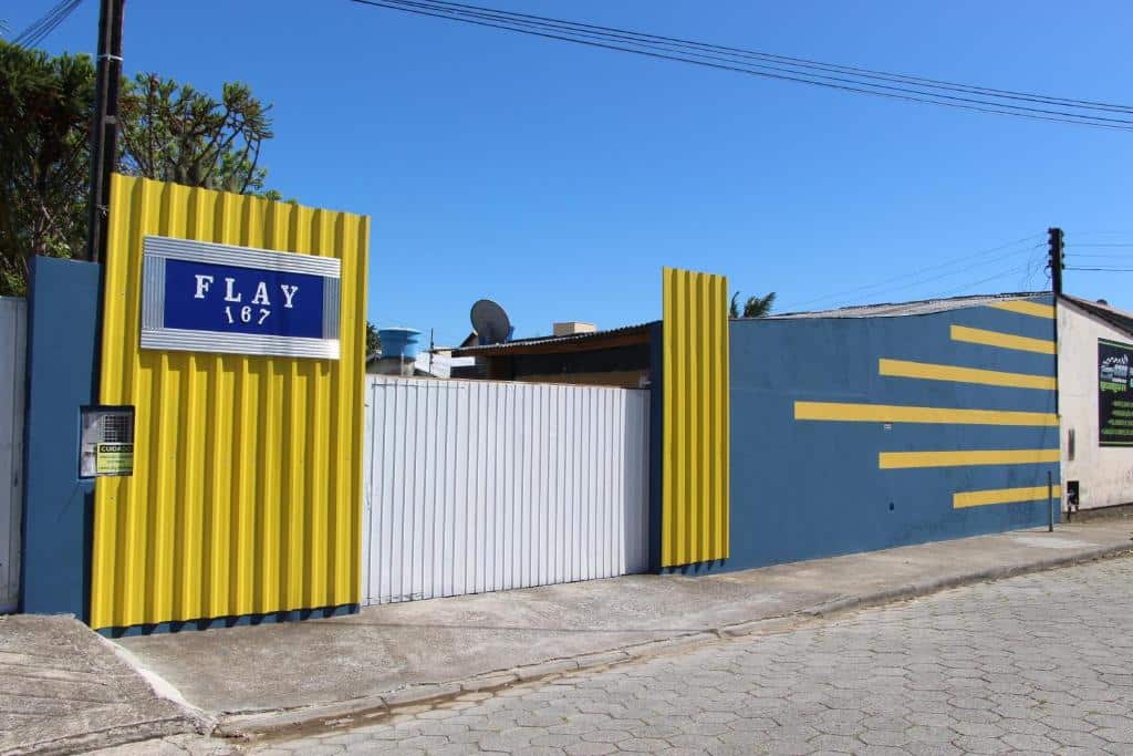 fachada da Pousada Flay 7 minutos perto do Aeroporto de Florianópolis, com placas em amarelo e parede cinza e o nome do local