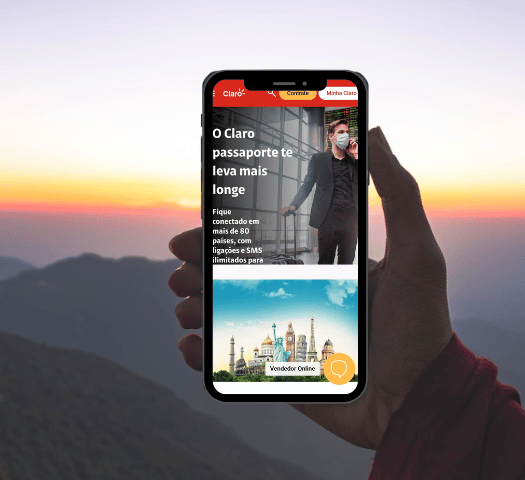 mão de uma pessoa segurando um celular com o print da página inicial do Passaporte Claro em detalhes vermelhos ao pôr do sol em meio a montanhas