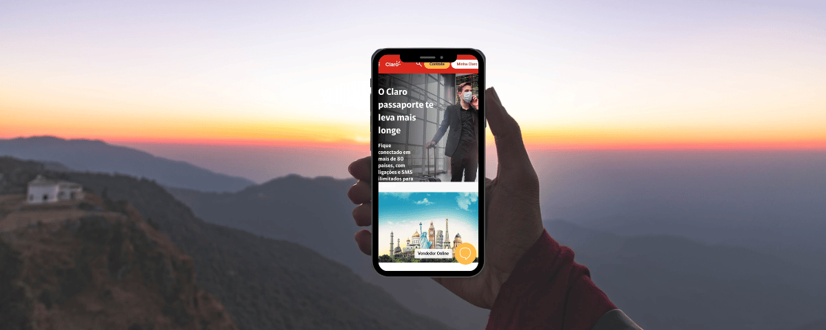 mão de uma pessoa segurando um celular com o print da página inicial do Passaporte Claro em detalhes vermelhos ao pôr do sol em meio a montanhas