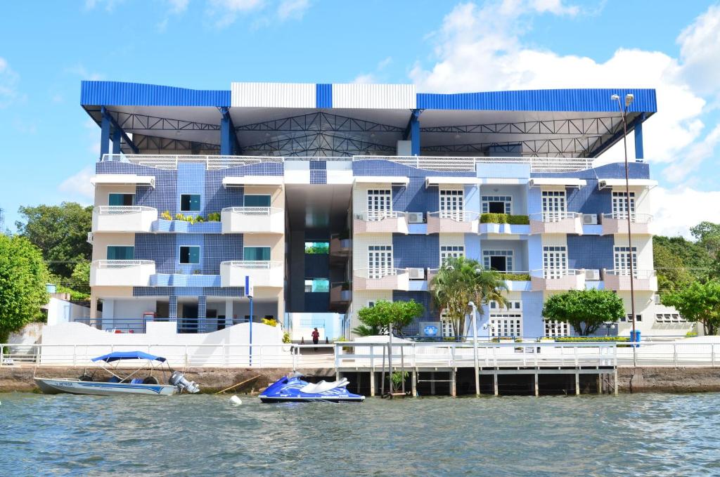 Vista da frente do Hotel Mirante Da Ilha durante o dia com um rio a frente e ao fundo o hotel com cores azuis e brancos com várias portas com sacadas. Representa Alter do Chão.